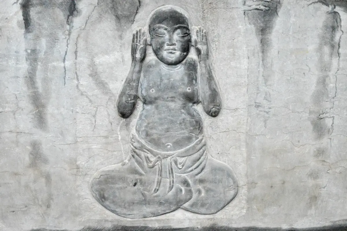 Un personnage assis en méditation, mains devant les oreilles.
