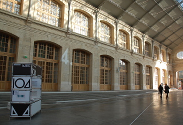 Grand hall lumineux avec grandes fenêtres en arche et deux personnes marchant au loin.