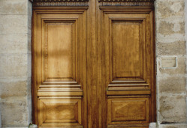 Porte cochère en bois avec panneaux sculptés encadrée par un mur en pierre.