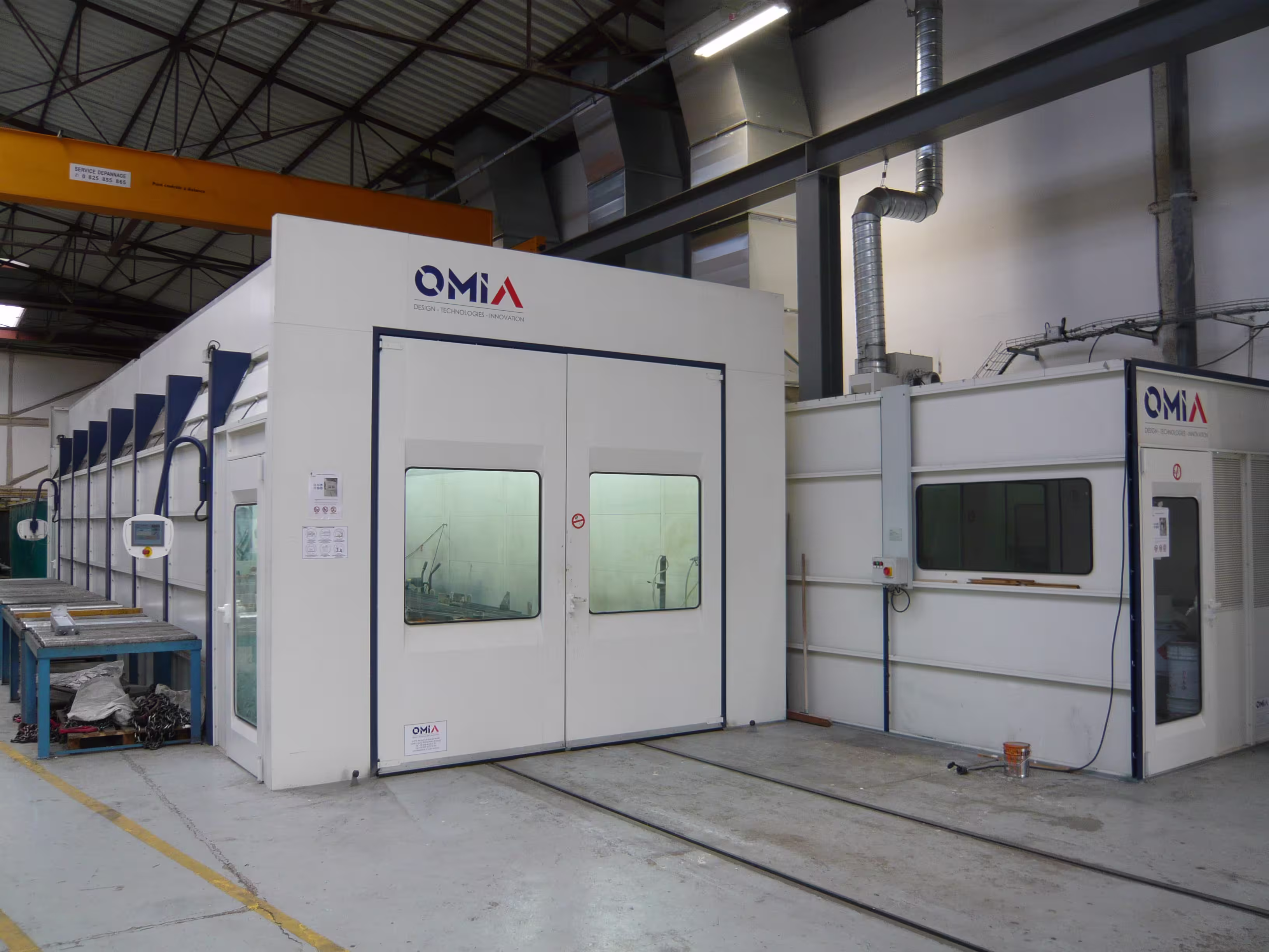 Grande cabine de peinture industrielle blanche avec fenêtres et porte double, installée dans un atelier spacieux.