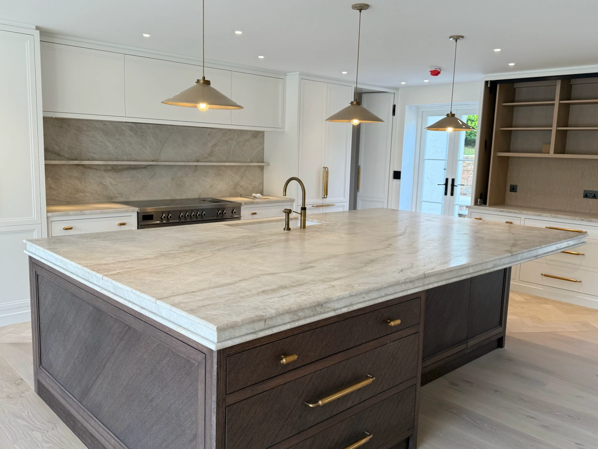 Modern kitchen with large marble island, dark wood cabinetry, white cabinets, brass fixtures, and three pendant lights.