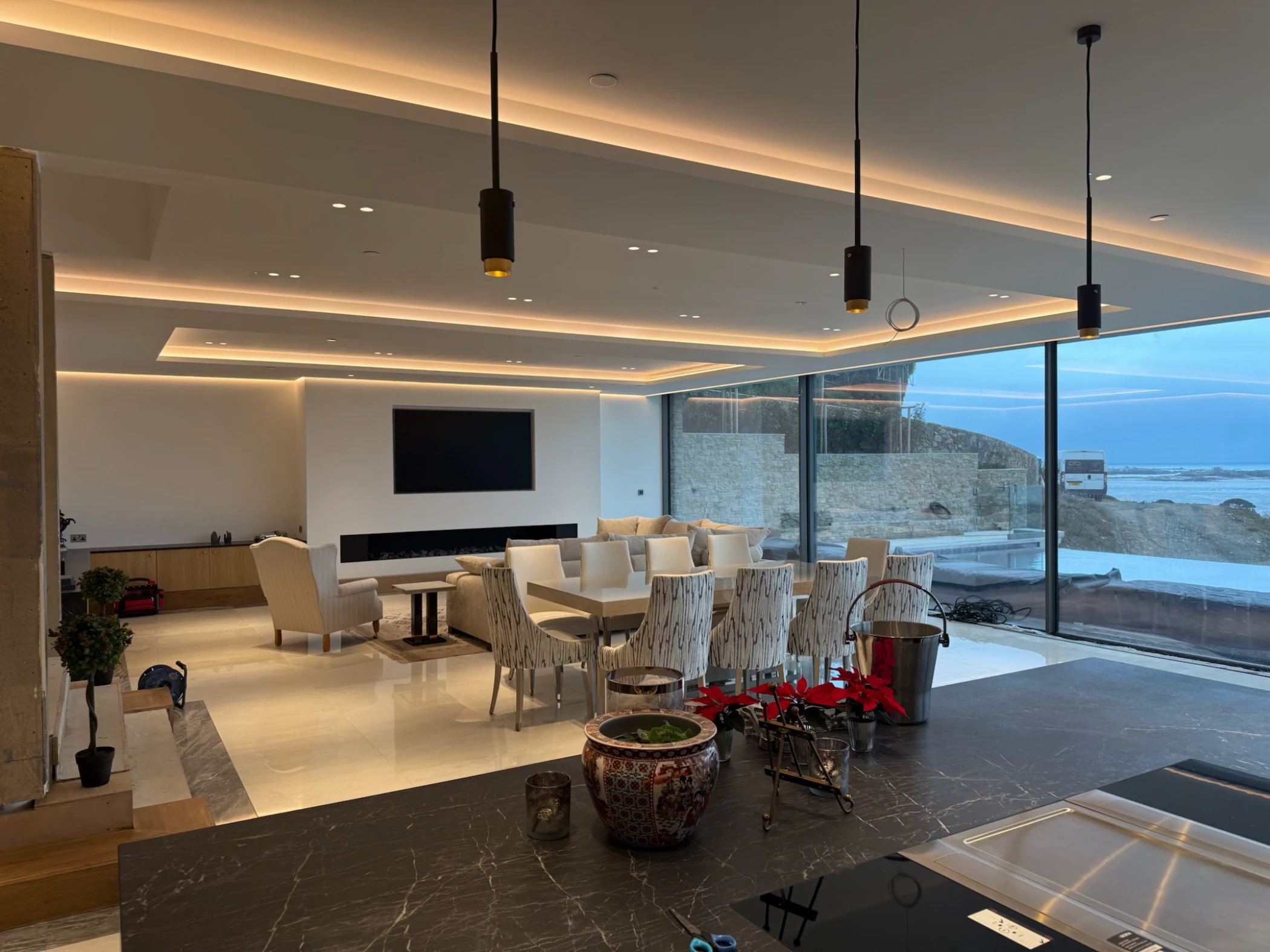 Modern open living and dining area with large windows overlooking an outdoor pool and a seaside view.