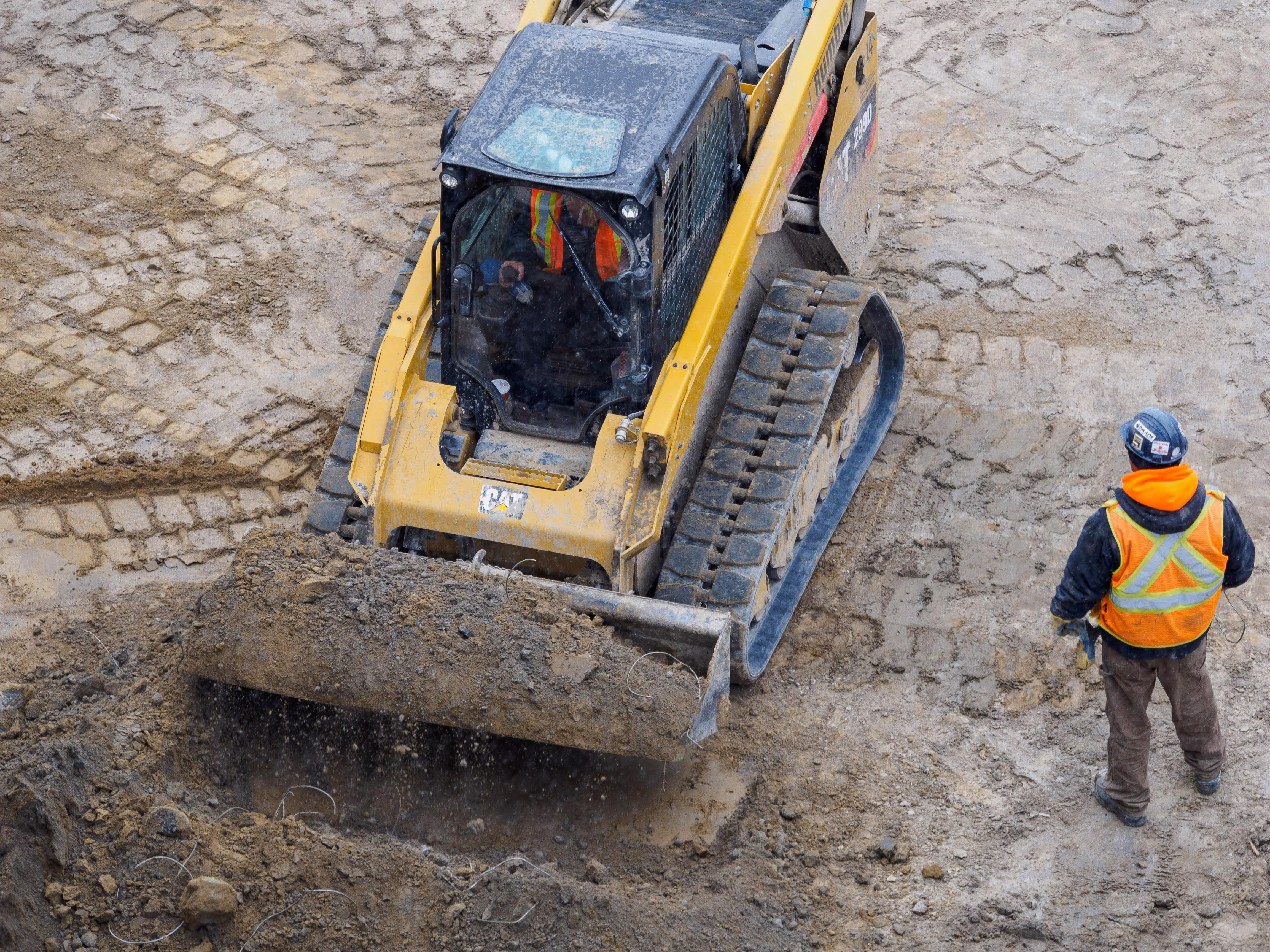 Skidsteer loader lifting some earth with a construction worker next to it