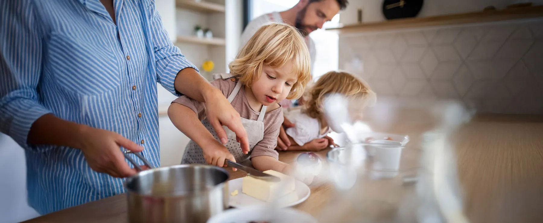 Eine Familie beim Backen. Ein Kind schneidet ein Stücke von der Butter ab.