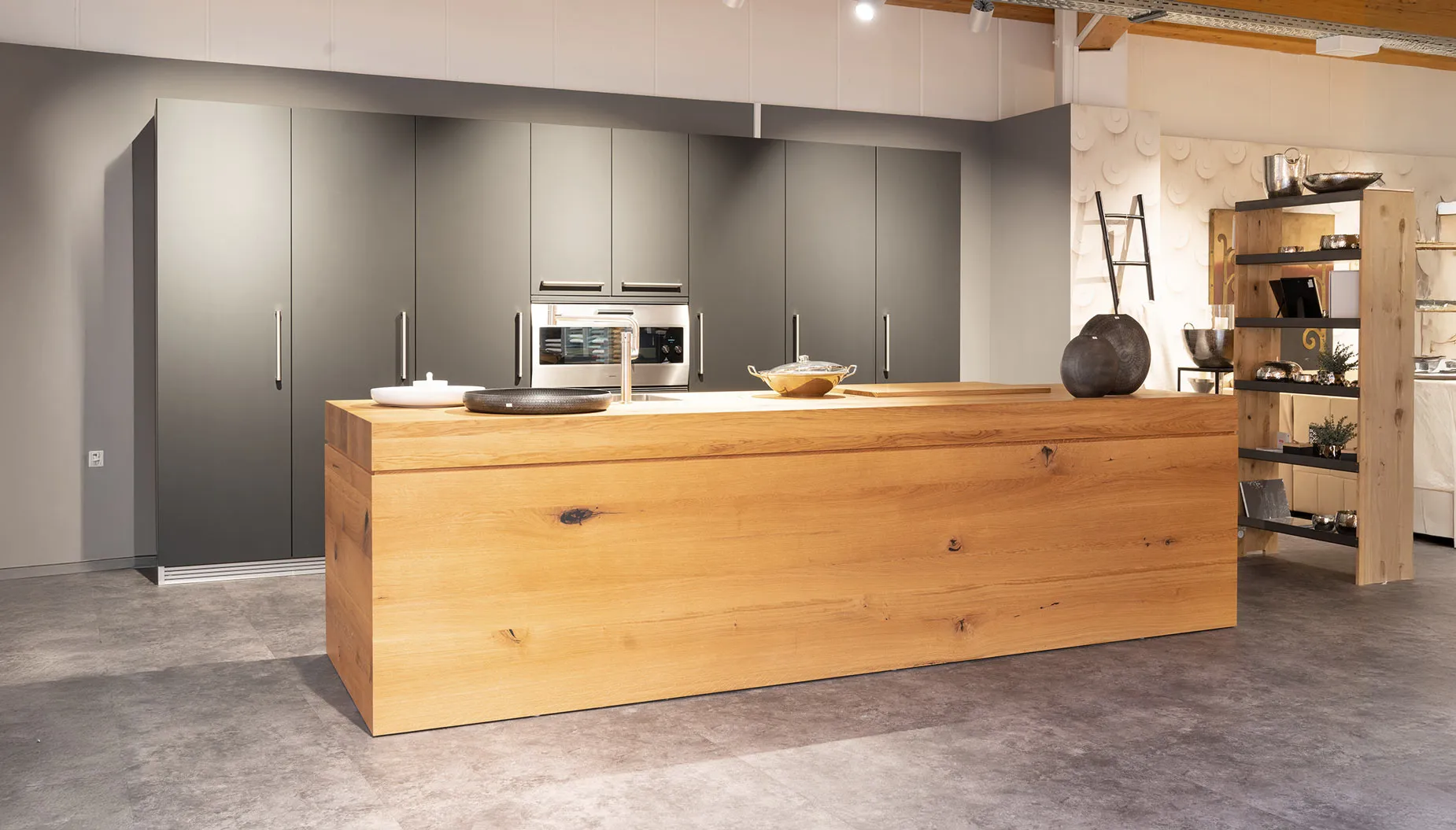 Moderne Küche mit dunklen Hochschränken und Kochinsel aus hellem Holz auf grauem Boden.