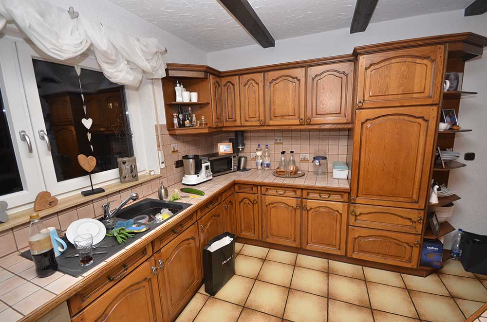 Rustikale Küche mit braunen Holzschränken, gefliestem Arbeitsbereich und sichtbaren Gebrauchsgegenständen.