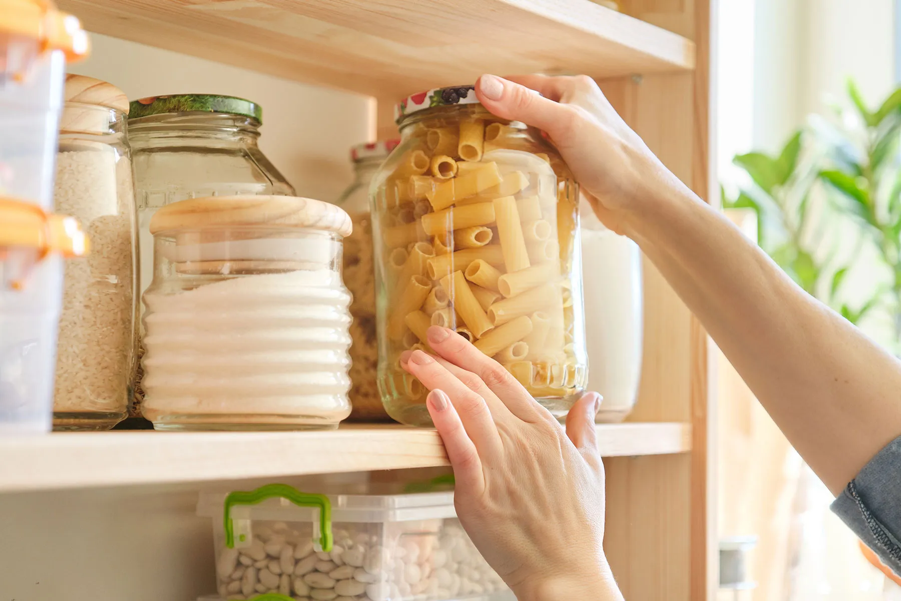 Eine Frau greift nach einem Glas mit Nudeln in einem Schrank voller Lebensmittel.