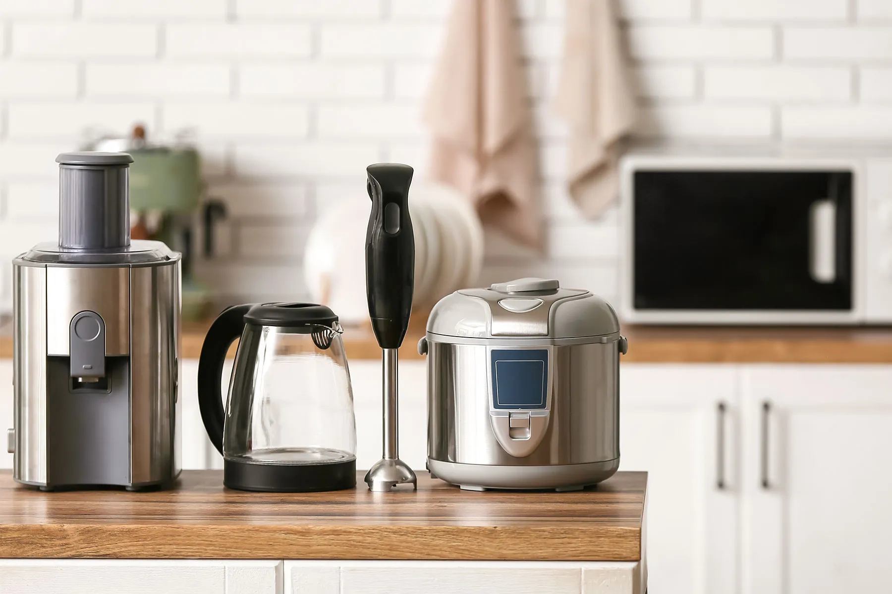 Ein Wasserkocher, ein Stabmixer und ein Thermomix stehen nebeneinander auf einer Holzarbeitsplatte in einer Küche.
