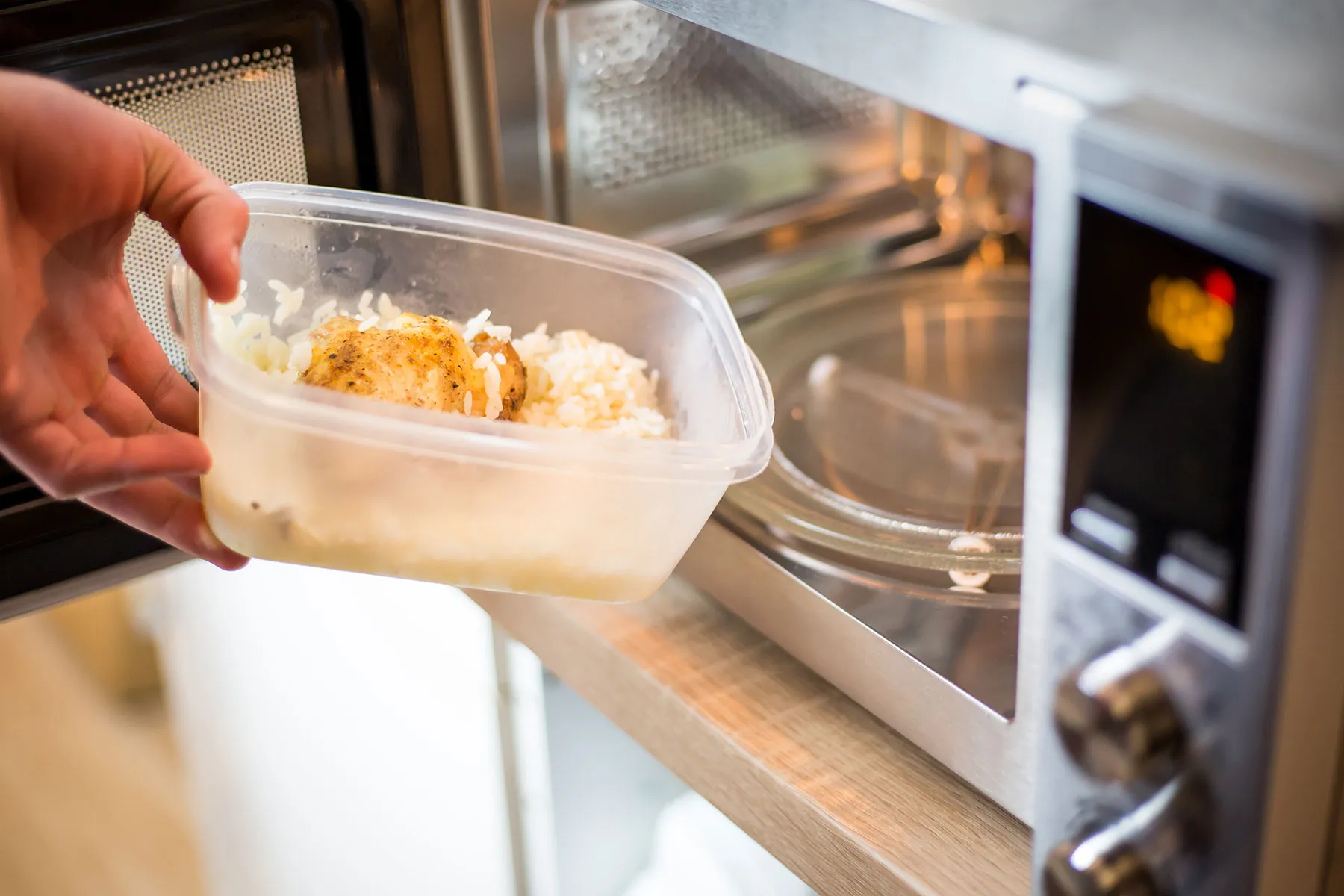 Eine Plastikschale mit Reis wird in eine Mikrowelle gestellt.