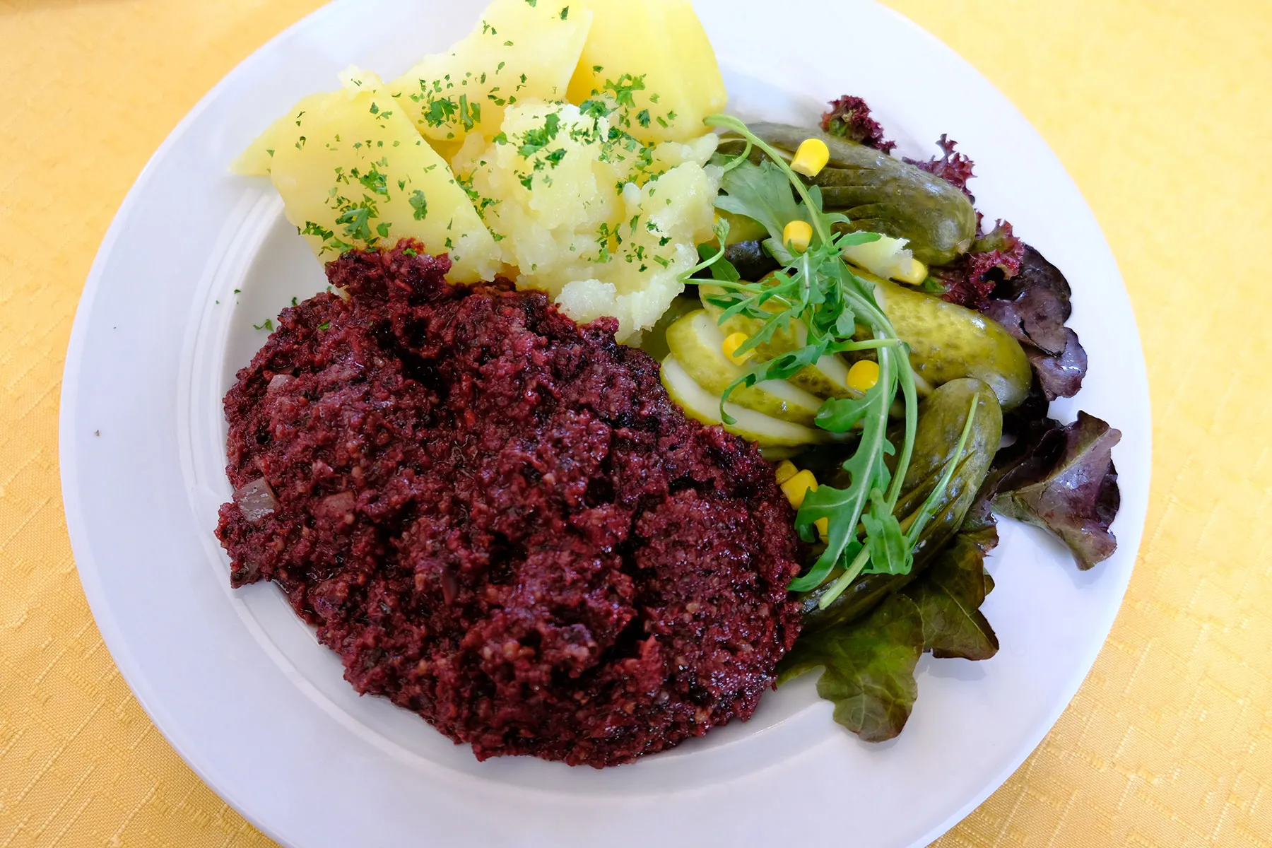 Ein Teller mit Kartoffeln, Gewürzgurken und Grützwurst.
