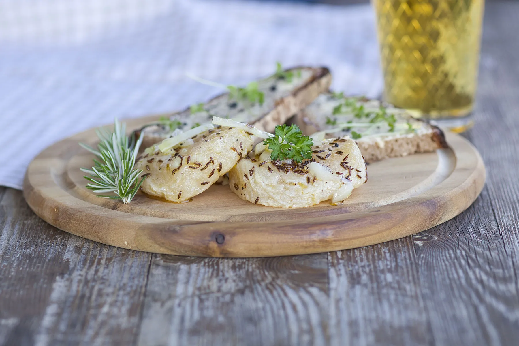 Ein Holzbrett mit Handkäs und zwei Schreiben Brot, dekoriert mit Rosmarin und Petersilie.