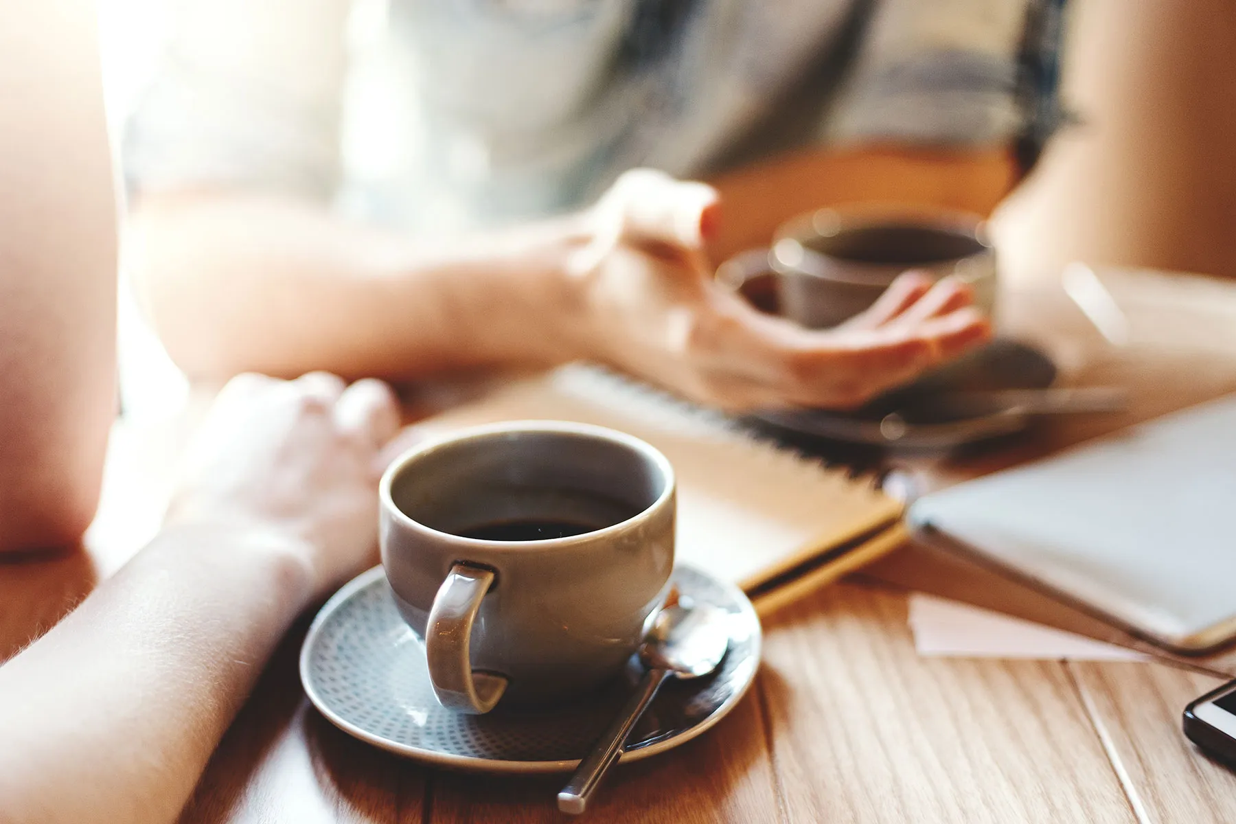 Eine Tasse Kaffee. Zwei Menschen unterhalten sich am Tisch.