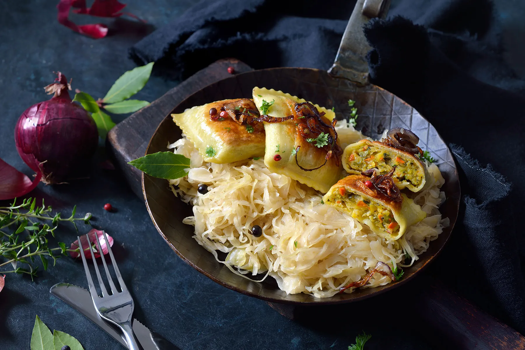 Eine Pfanne voll mit Maultaschen auf einem dunklen Tisch.