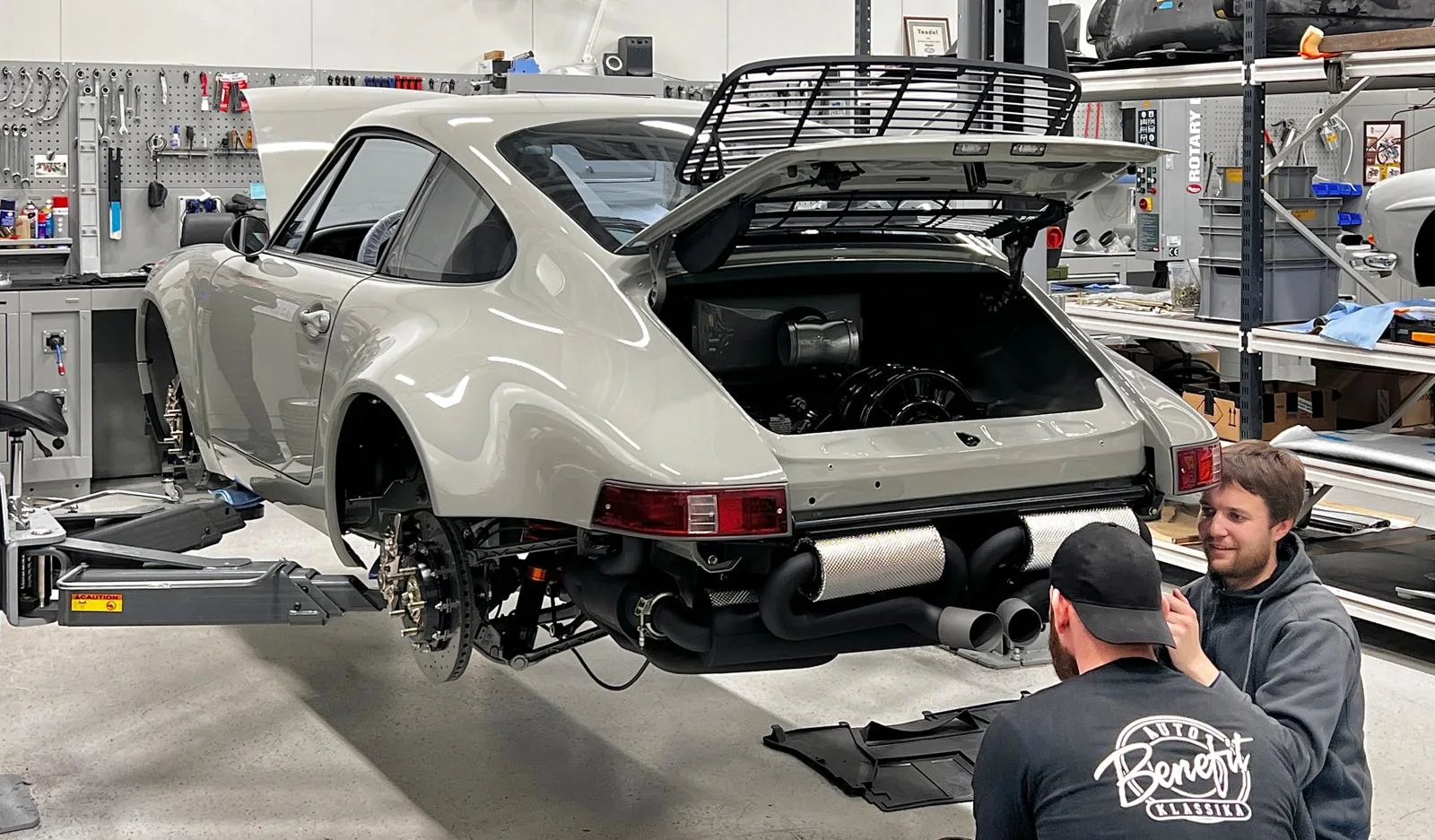 A picture of an Kalmar Automotive Porsche 911 restomod on an lift and two guys working on it