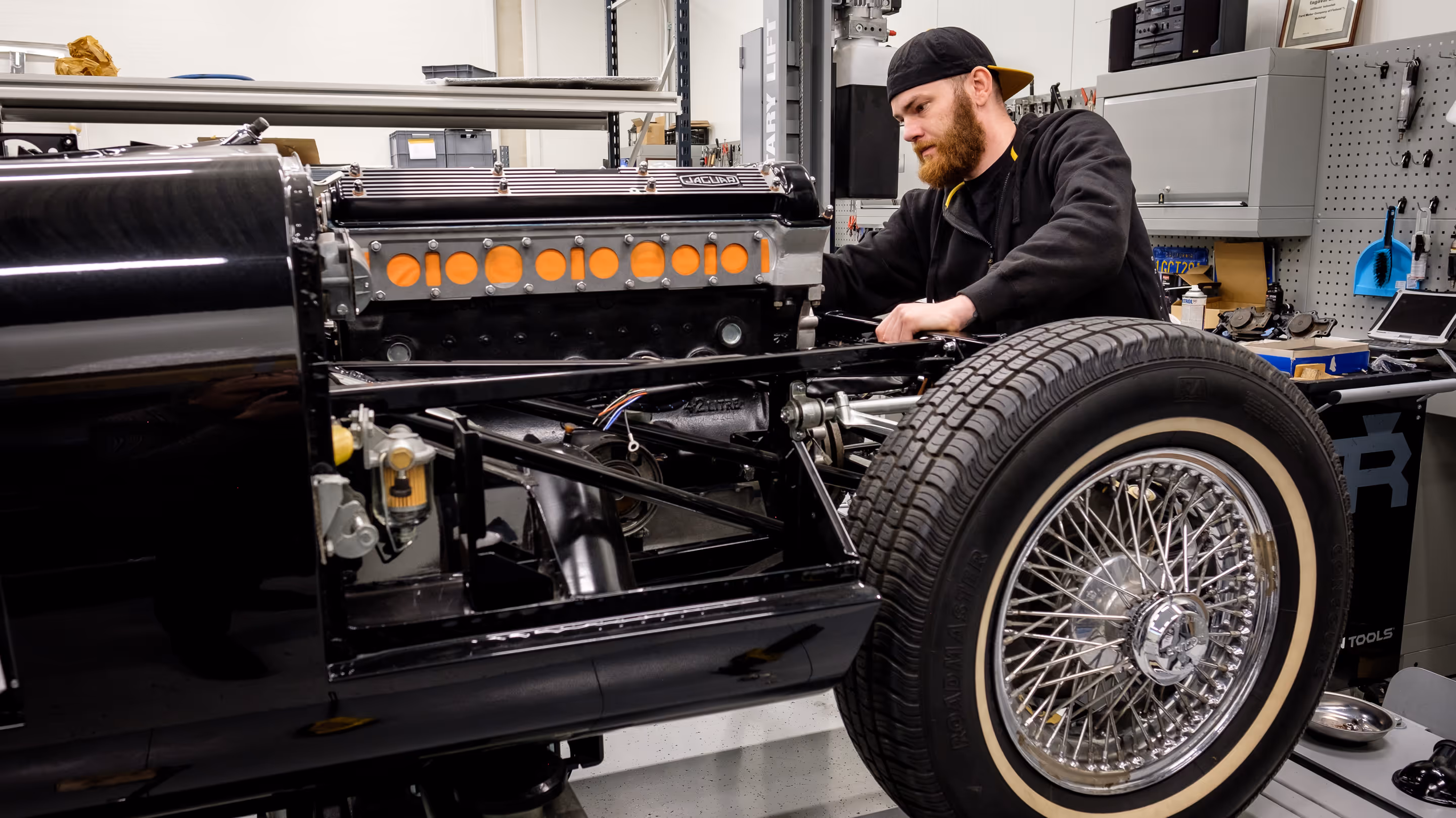 A mechanic servicing a black Jaguar E-type's engine