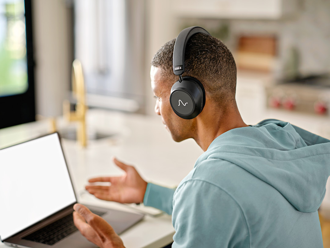 Person working at a laptop in a kitchen, wearing Neurable One headphones