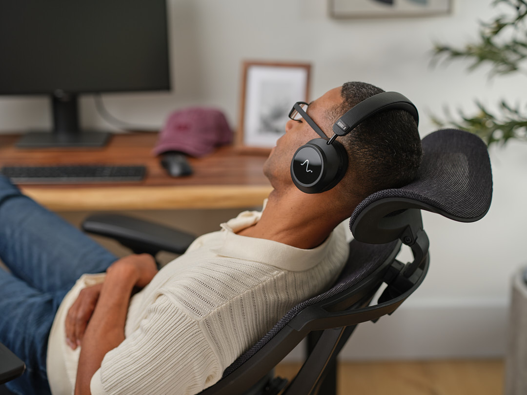A man leaning back in his desk chair with his eyes closed, wearing Neurable One