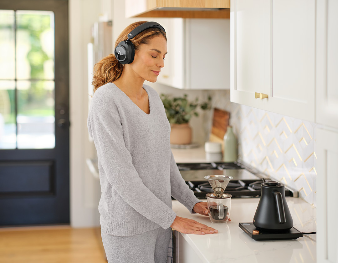 A woman wearing Neurable One while making pour-over coffee in her kitchen