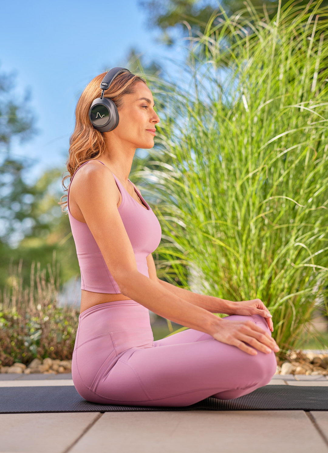 A woman meditating outdoors on a mat, wearing Neurable One headphones