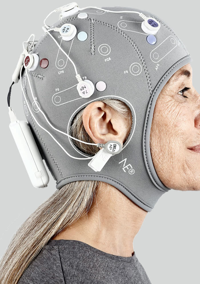 A person wearing a grey laboratory EEG cap covered in wired electrodes.
