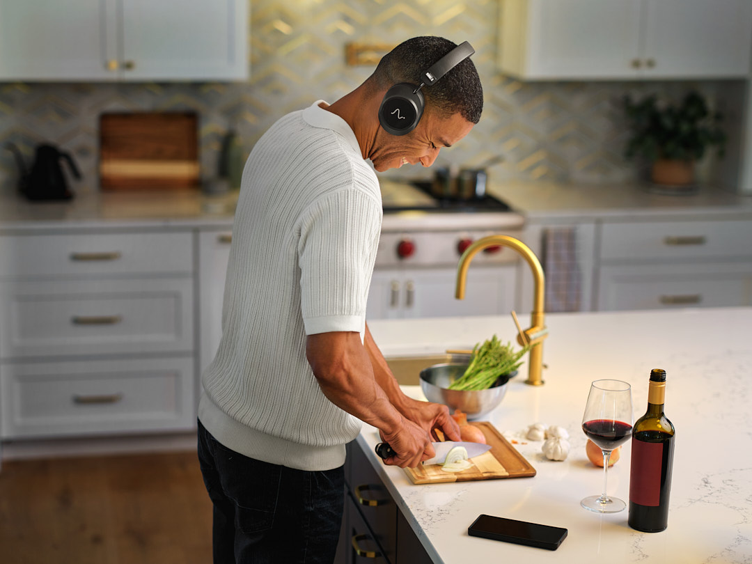 A man wearing Neurable One headphones while chopping vegetables in a kitchen.