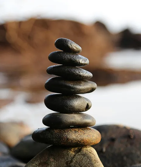 Stones stacked and balanced against a blurry backdrop of water and cliffs