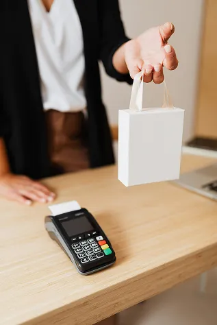 woman at counter standing over a card machine handing over a white shopping bag