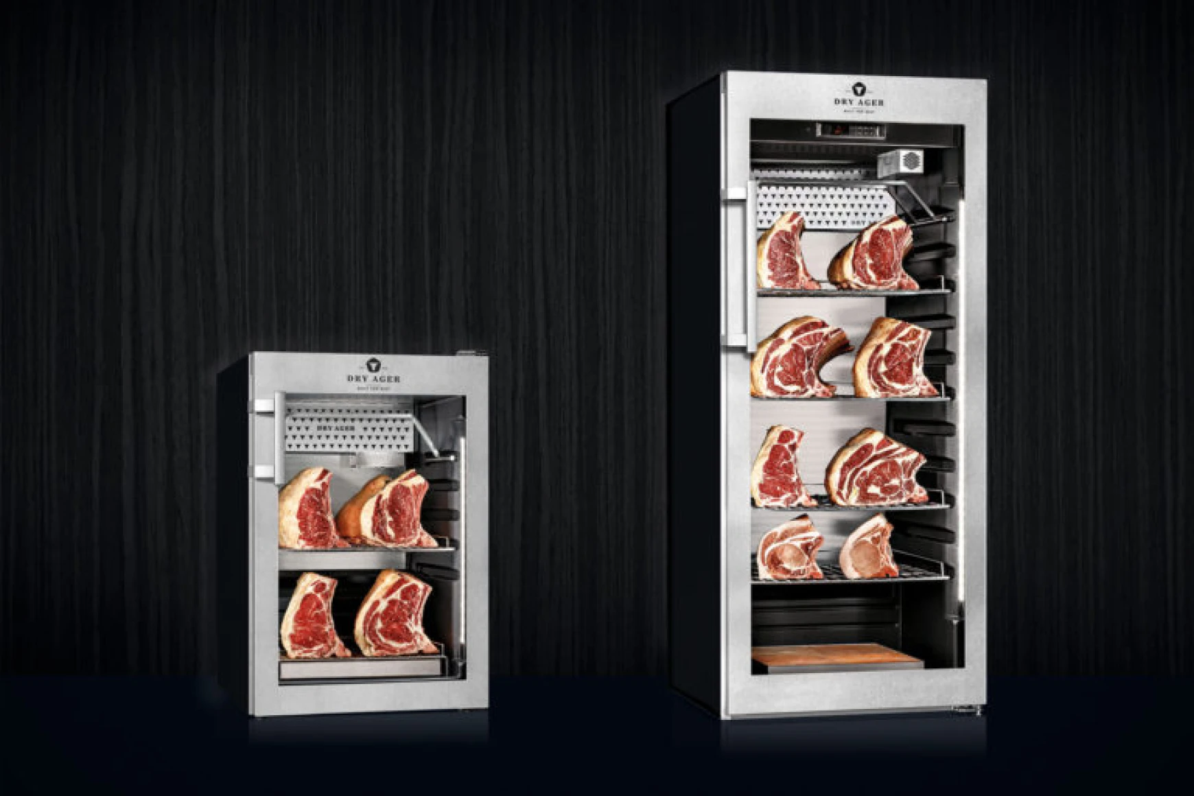 Two stainless steel dry aging cabinets with multiple shelves holding large cuts of marbled raw meat.