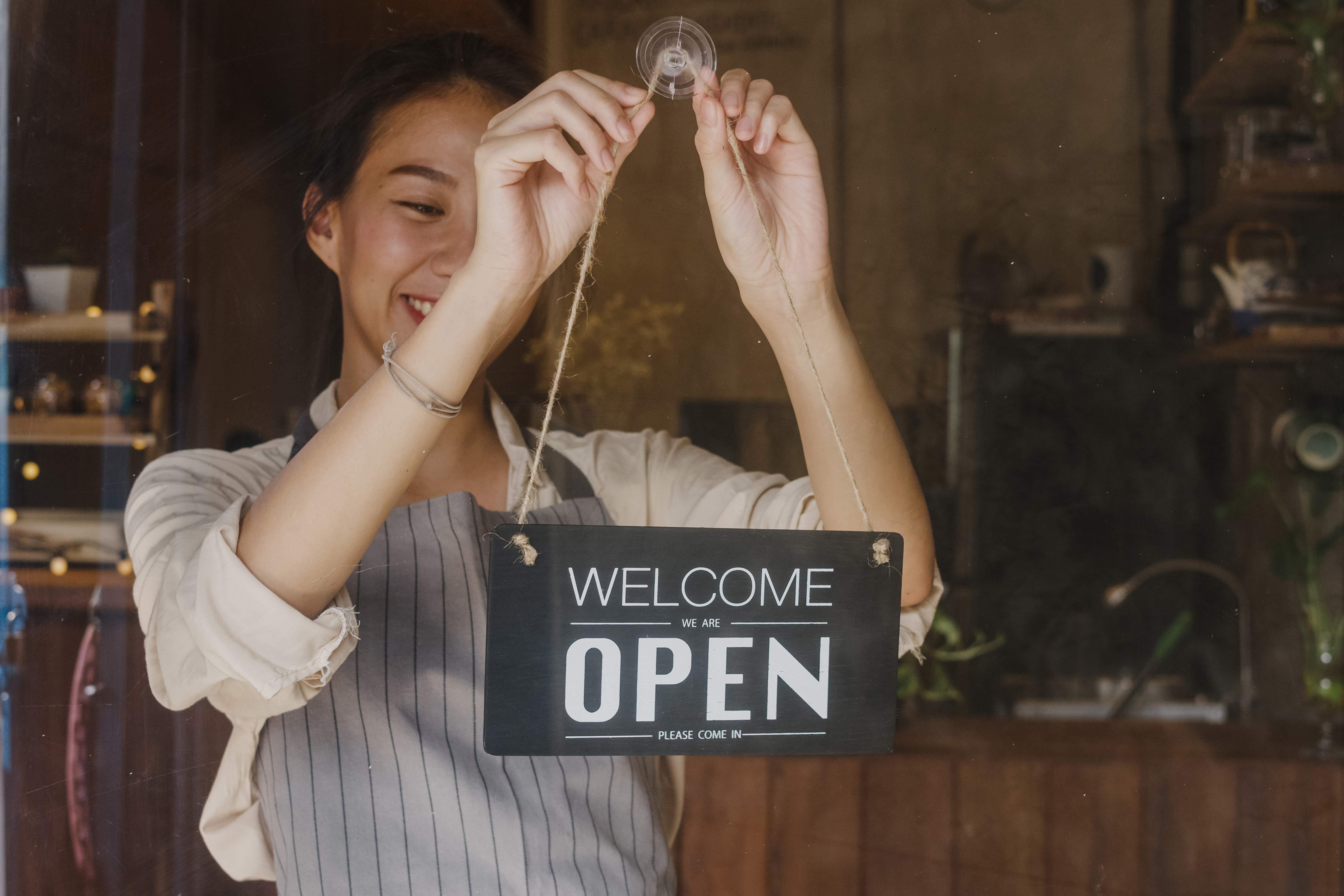 Stressed man sitting at a table with a laptop, coffee cup, and open planner while a woman and child play in the background of a modern living room.