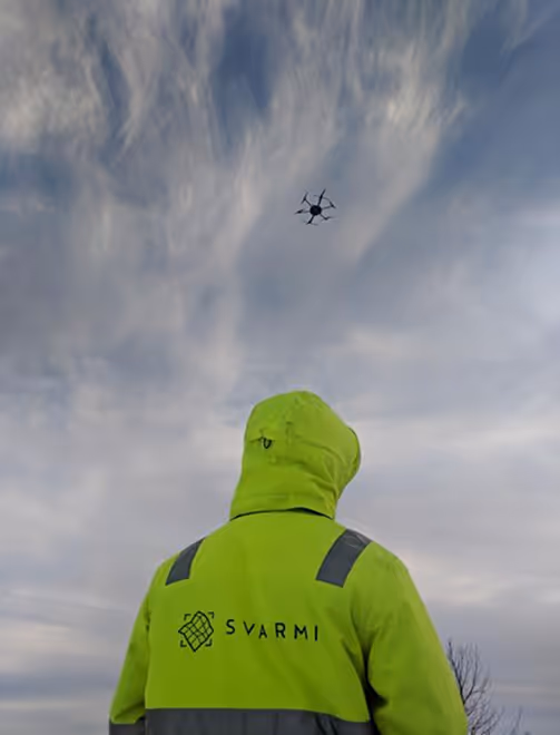 Person in Svarmi high vis jacket with a drone flying overhead | Svarmi