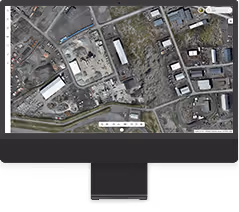 Aerial satellite map view of an industrial and residential area displayed on an iMac screen.