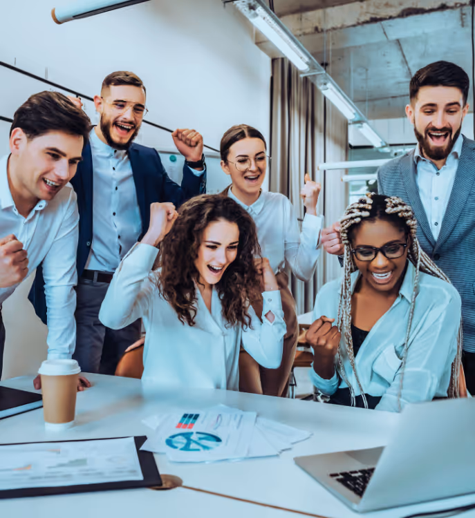 Group of happy young professionals celebrating success around a laptop in a modern office.