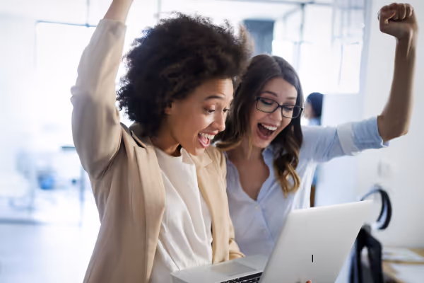 Two women happy and excited at the results they're seeing on their work computer.