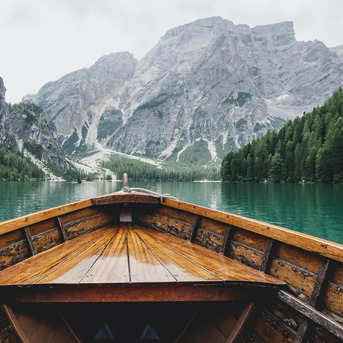 View from a wooden boat on a turquoise lake toward a mountain landscape.