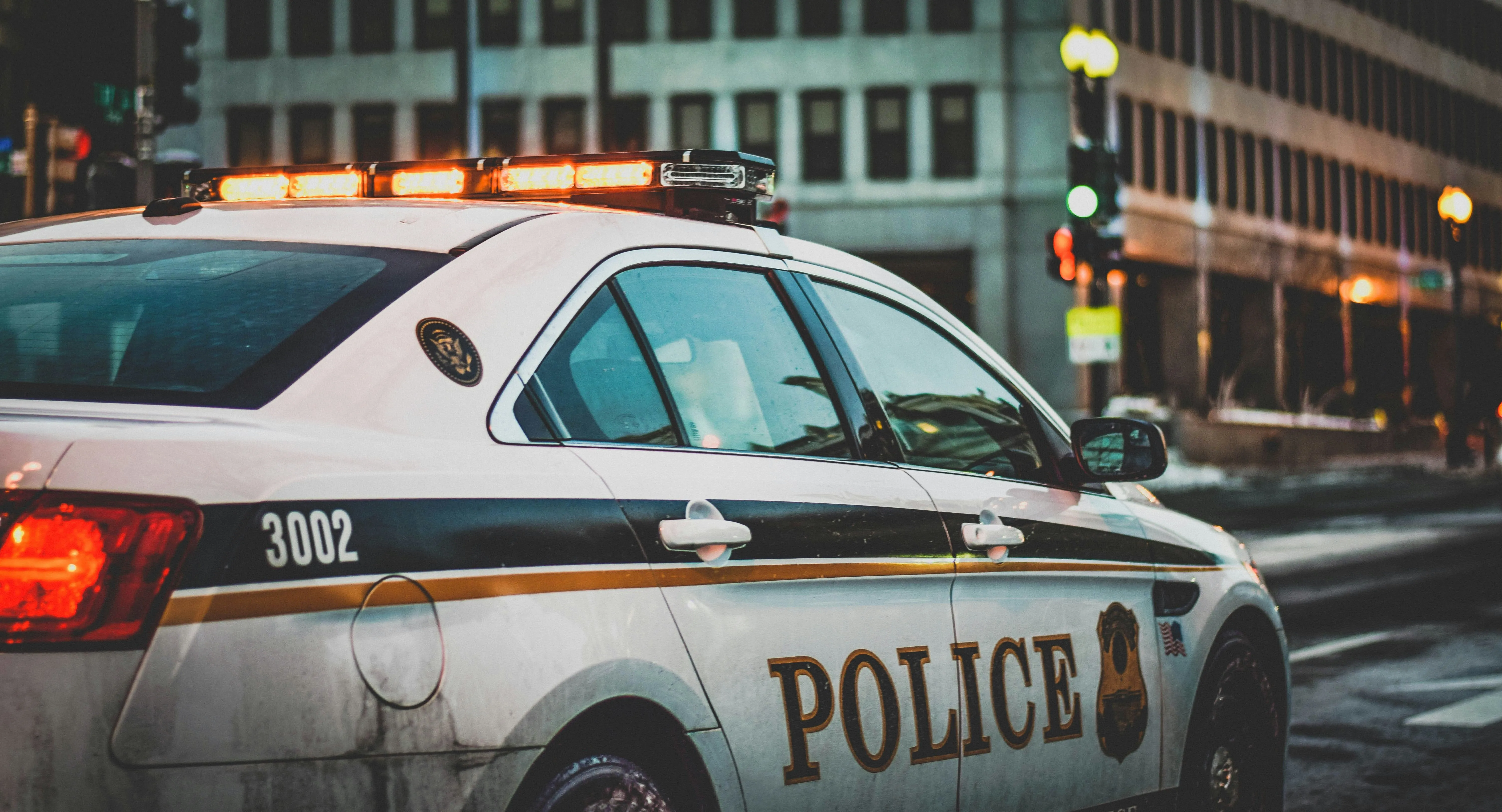 Police car with lights on parked on a city street at dusk, representing active law enforcement or patrol activity.