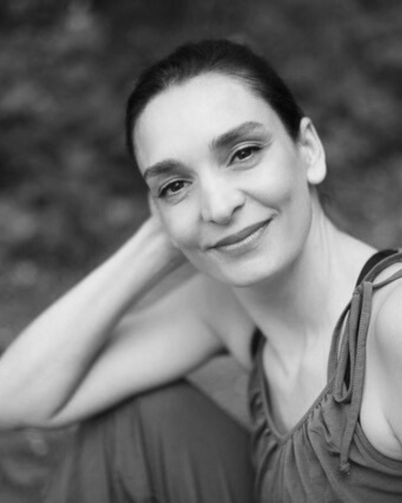 Black and white portrait of a woman smiling gently, resting her head on her hand.
