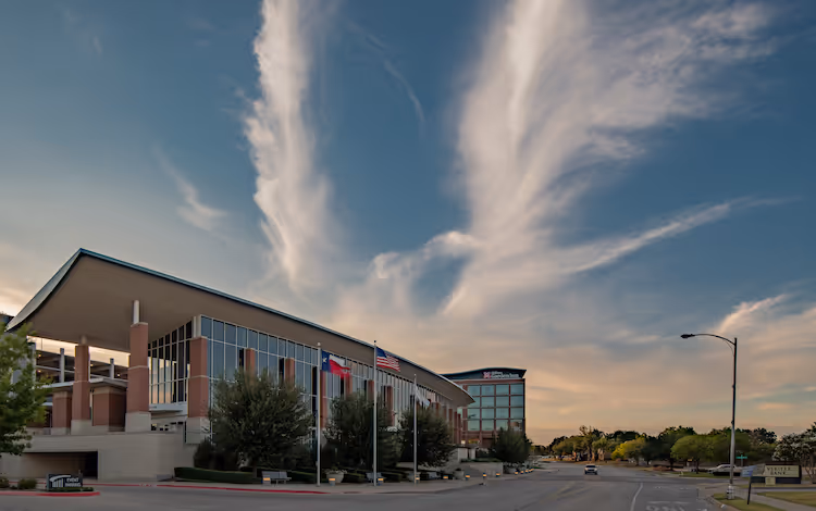 Modern government building with flags under dramatic wispy cloud-filled sky