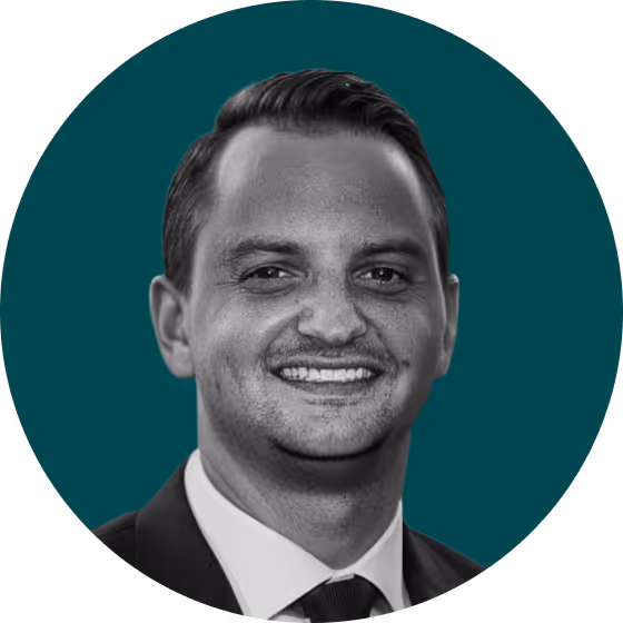 Smiling man with dark hair in a suit and tie against a teal background.