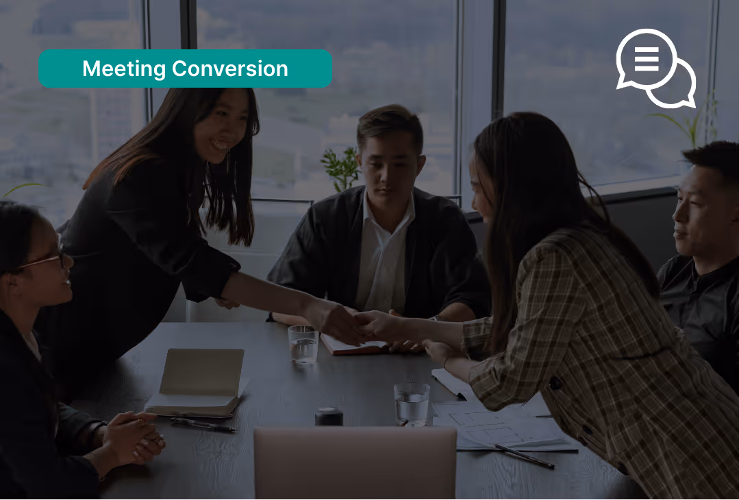 Two women shaking hands across a conference table during a business meeting with three others seated nearby.
