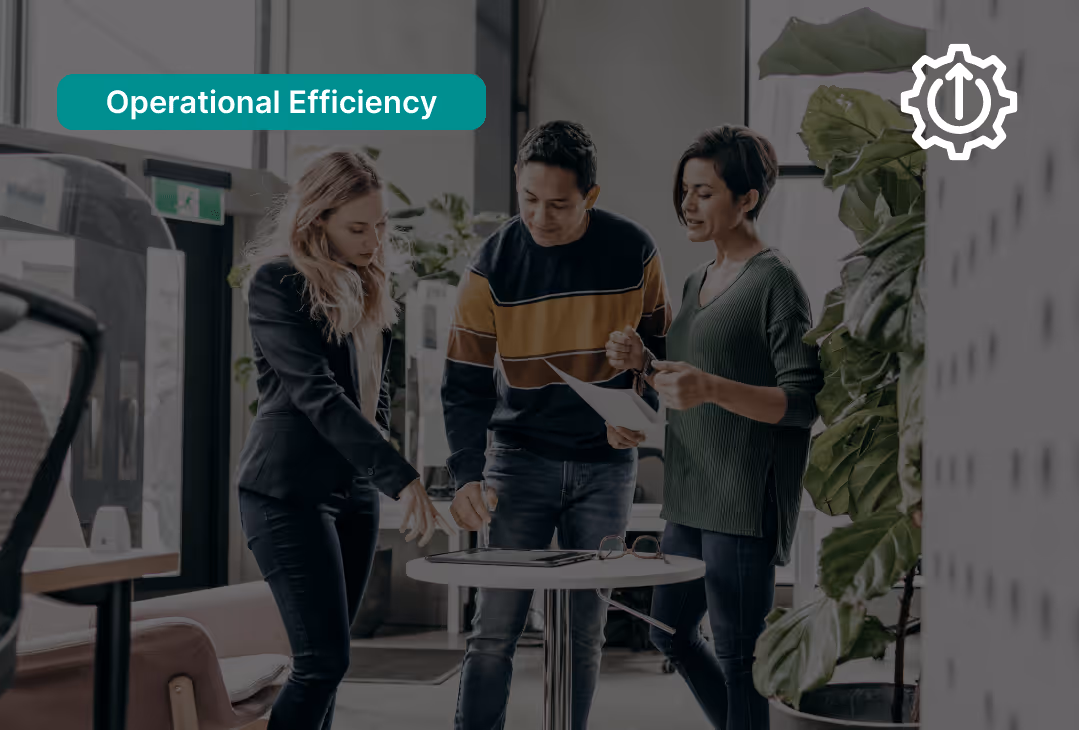 Three colleagues discussing documents around a small round table in a modern office with plants.