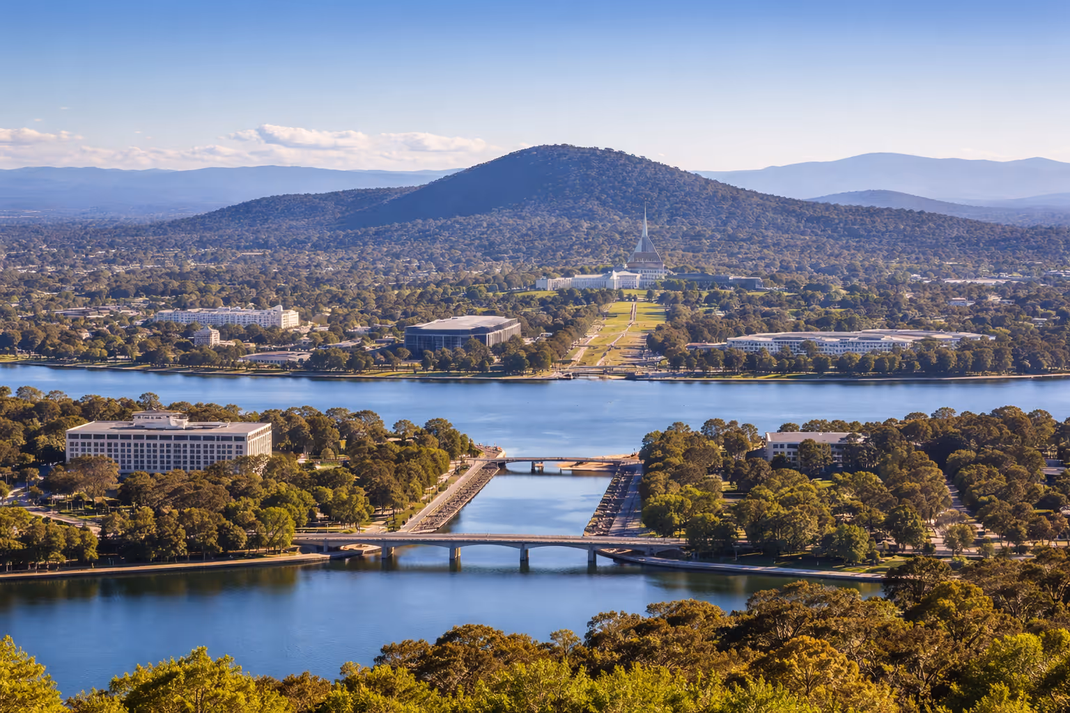 View of a river, bridges, green trees, buildings, and a large hill with a distinct building on top.