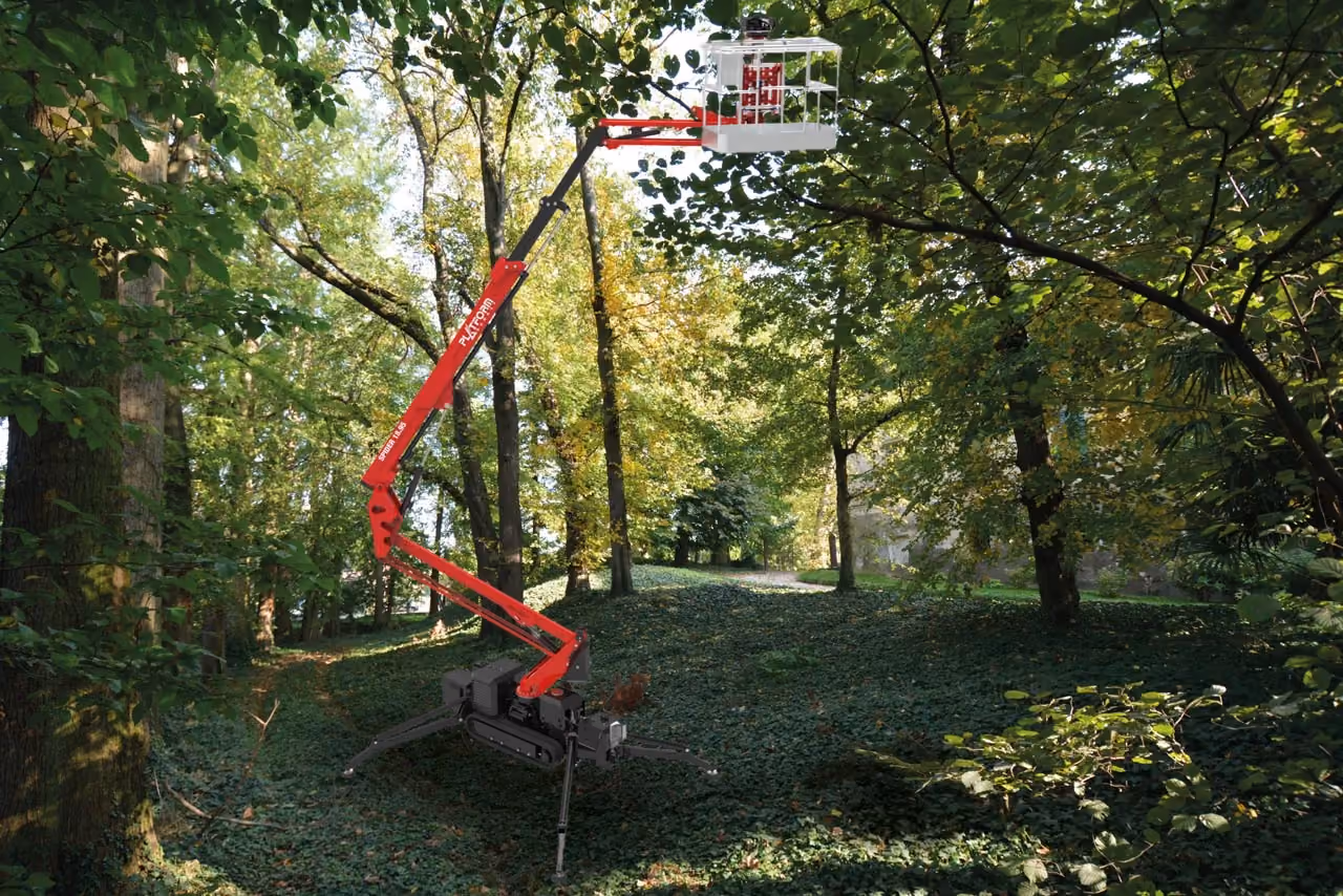 Red and black articulated lift platform extended high among leafy trees in a green forest area.