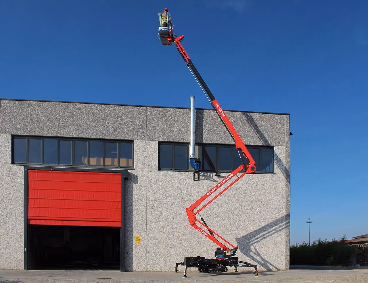 Worker in a raised cherry picker attached to a red articulating boom lift outside a building.