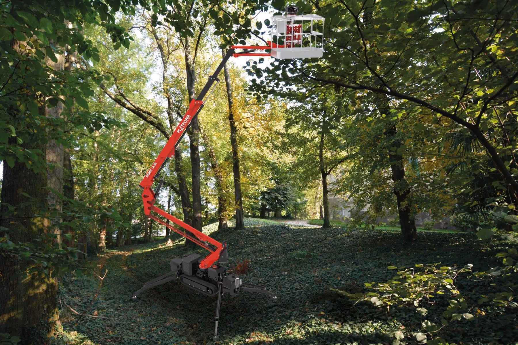 Red and black articulated lift with basket extended in a green forested area with sunlight.