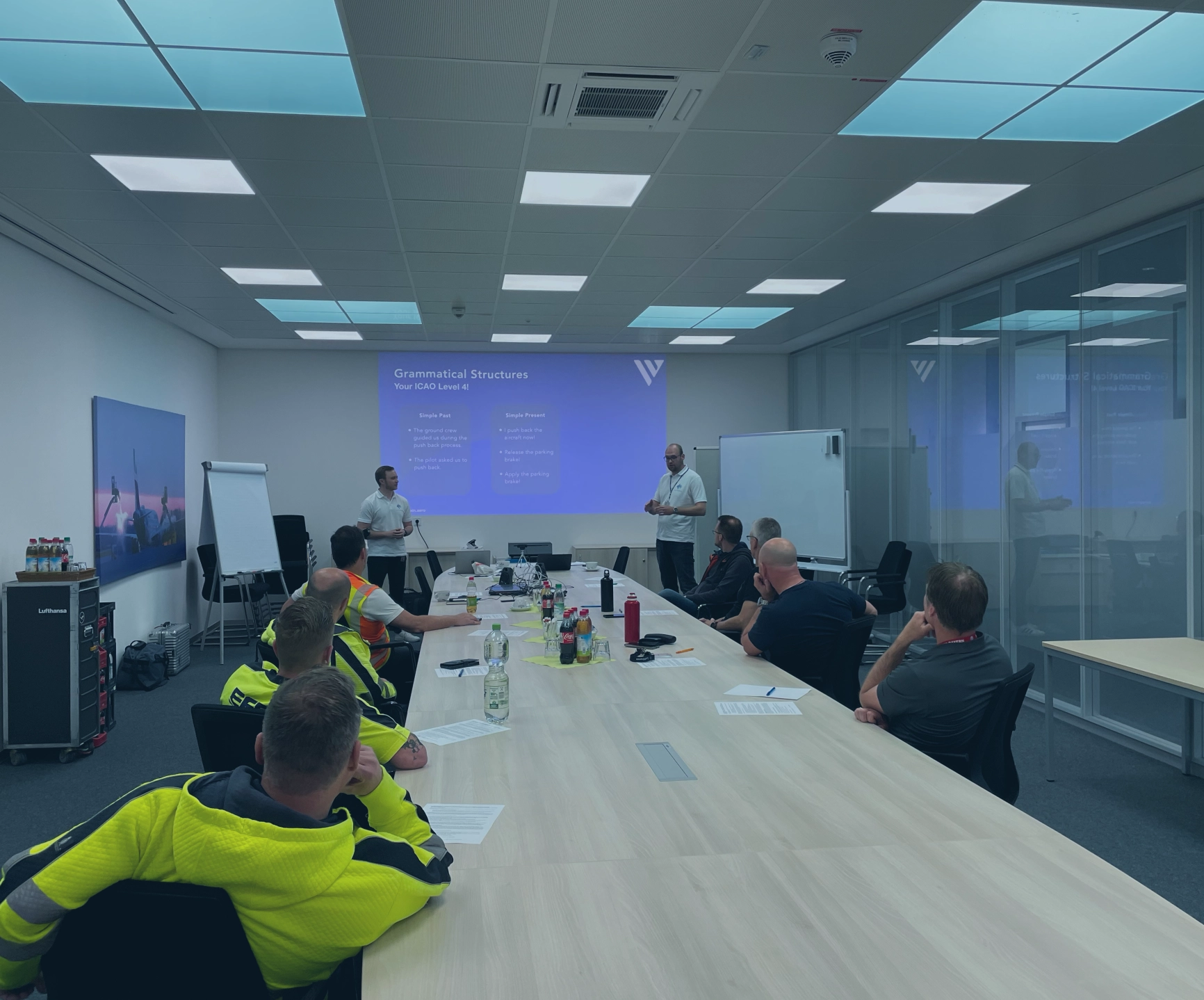 A group of people attend a training session on grammatical structures in a modern conference room.