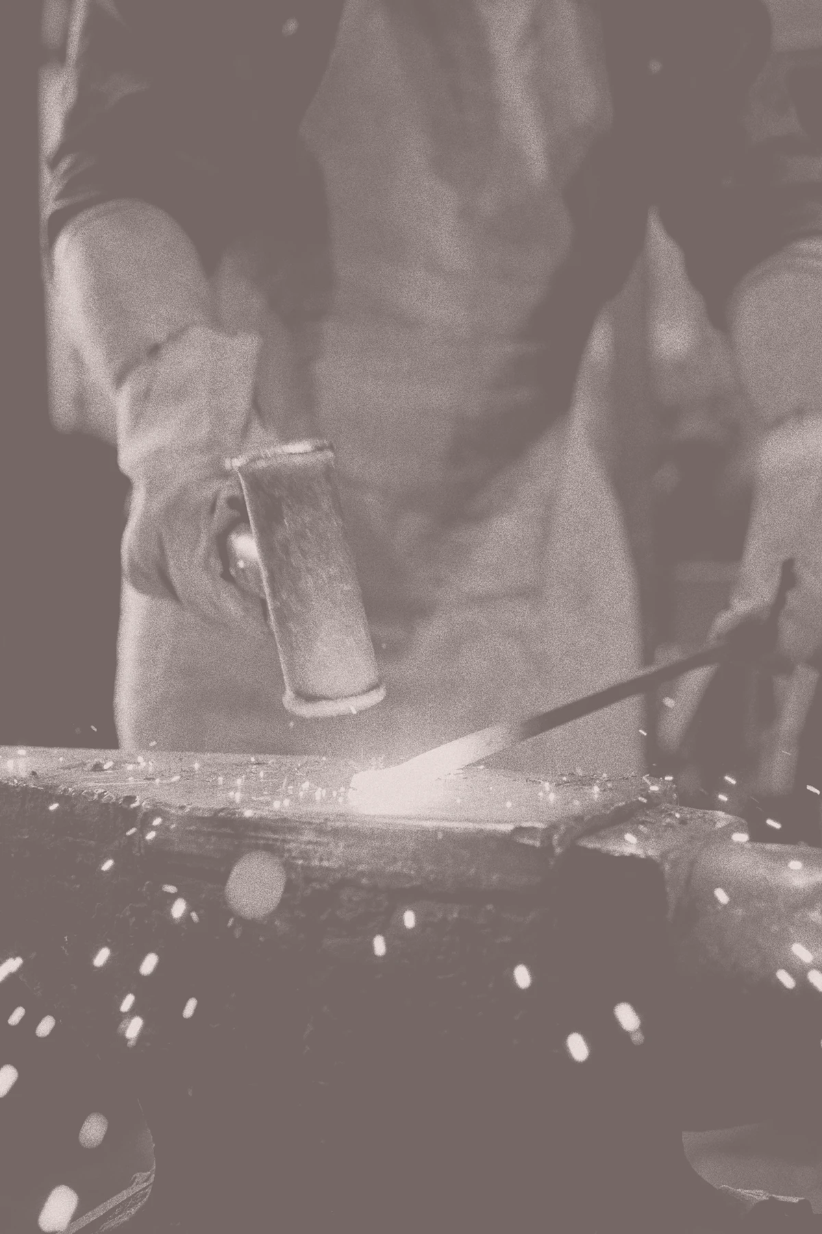 Close-up of a blacksmith hammering hot metal on an anvil, with sparks flying across the foreground.