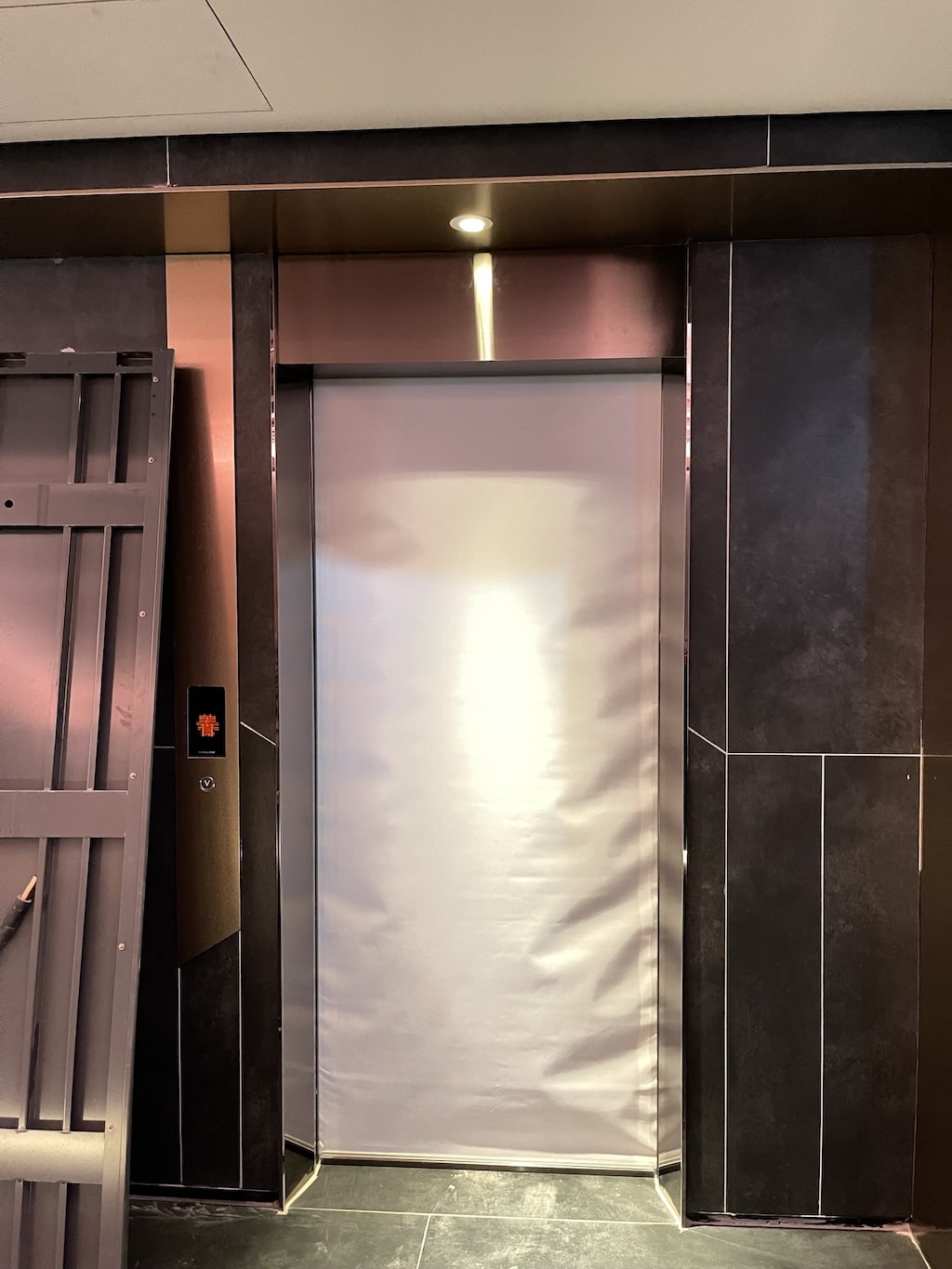 An elevator door covered by a silver protective curtain in a dark tiled hallway.