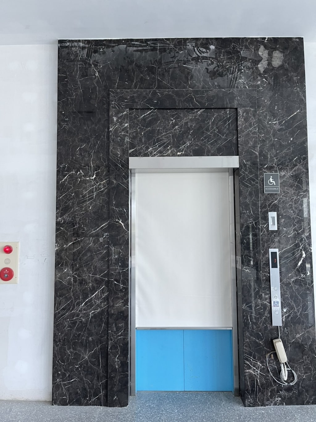 Disabled accessible elevator with closed doors framed by black marble walls and a wall-mounted phone.