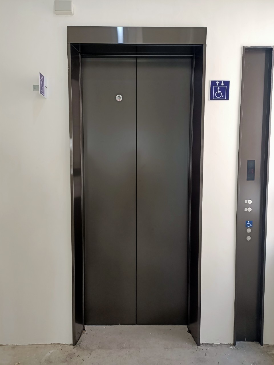 Closed metallic elevator doors with wheelchair accessible signs on a white wall.