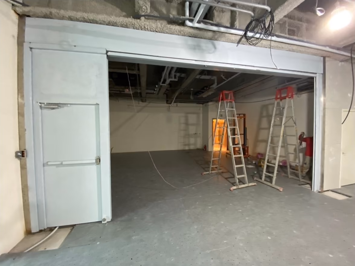 室內建築施工現場，有兩架梯子和一扇帶標誌的白色門，燈光昏暗。